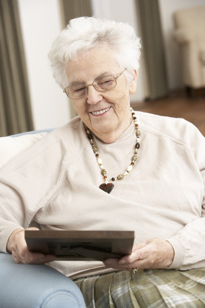 Senior Woman Looking At Photograph In Frame - Foto, imagen