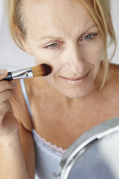 Mid age woman putting on make-up - Fotó, kép