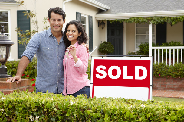 Hispanic couple outside home with sold sign - 写真・画像