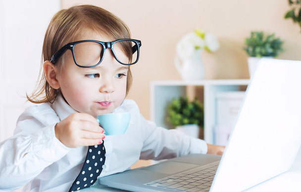 дівчинка-малюк п'є каву під час використання ноутбука
 - Фото, зображення