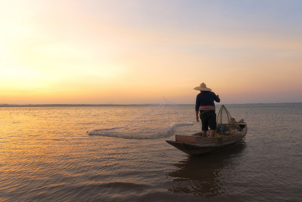 Pêcheur asiatique avec son bateau en bois va attraper des poissons d'eau douce dans la rivière de la nature au début de l'heure du lever du soleil
 - Photo, image