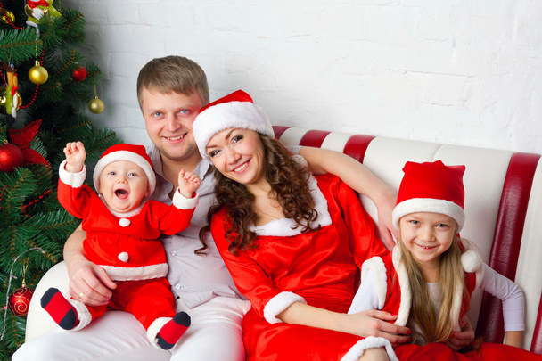 Ευτυχισμένη οικογένεια σε Santa κοστούμια που περιμένουν για τα Χριστούγεννα. - Φωτογραφία, εικόνα