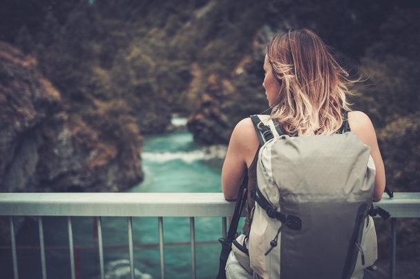 Wanderin mit Rucksack auf der Brücke über einen wilden Gebirgsfluss. - Foto, Bild