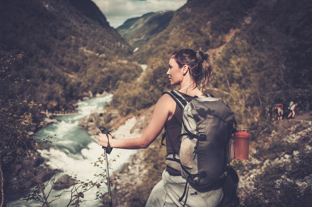 Жінка ходить з рюкзаком, що стоїть на краю скелі з епічним видом на дику гірську річку
. - Фото, зображення