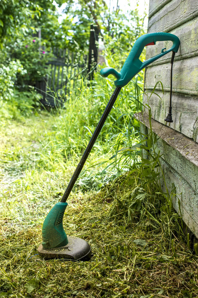 cortador de césped eléctrico se encuentra en el jardín cerca de la casa
 - Foto, Imagen