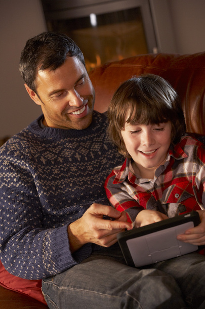 Father And Son Using Tablet Computer By Cosy Log Fire - 写真・画像