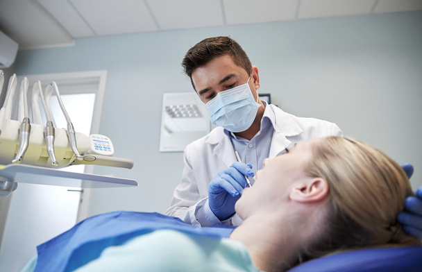 male dentist in mask checking female patient teeth - Foto, afbeelding