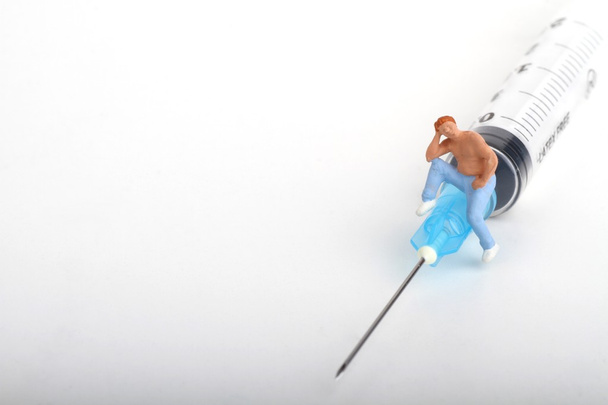 miniature figurine of a person sitting on a big syringe : therapy or drug addiction concept. - Photo, Image