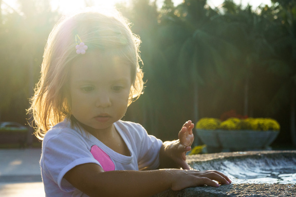 beautiful little girl washing her hands in the fountain.On the Sunset. serious thoughtful face. - 写真・画像