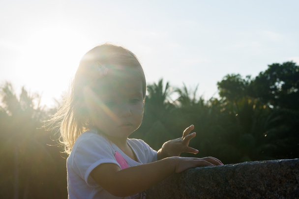 beautiful little girl washing her hands in the fountain.On the Sunset. serious thoughtful face. - Zdjęcie, obraz