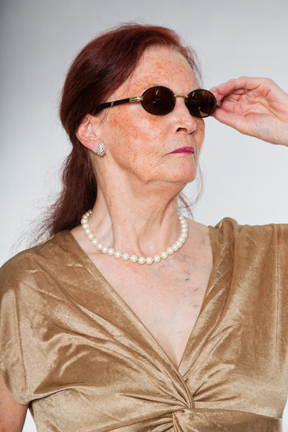 Ritratto di bella donna anziana che indossa occhiali da sole con viso espressivo che mostra emozioni. Si comporta da giovane. Studio girato isolato su sfondo grigio
. - Foto, immagini