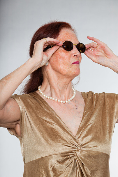 Portrait de belle femme âgée portant des lunettes de soleil avec un visage expressif montrant des émotions. Agir jeune. Studio tourné isolé sur fond gris
. - Photo, image