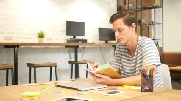 Młody mężczyzna pisania w notebooku z piórem, nowoczesny Loft Office - Materiał filmowy, wideo