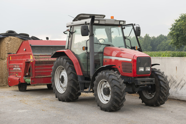 Tractor rojo con difusor de alimentación de ganado rojo
 - Foto, Imagen