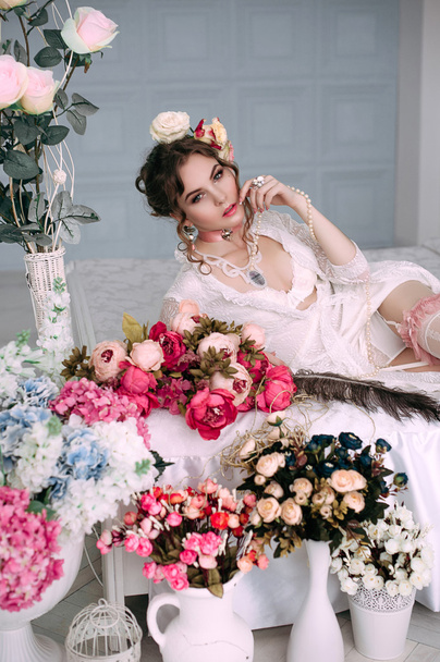 Mulher sexy jovem bonita sentada na cama branca, vestindo vestido de renda branca, cabelo decorado com flores. Maquiagem perfeita. Moda de beleza. Cílios. Estúdio retocado tiro
.  - Foto, Imagem