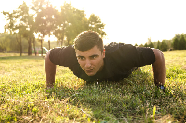 Close up of a man doing pushups on the grass with the horizon in the background. - Fotoğraf, Görsel
