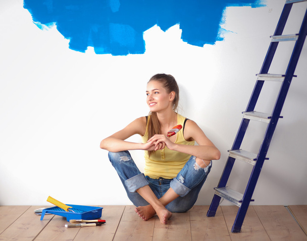 πορτρέτο του ζωγράφου γυναίκα που κάθεται στο πάτωμα κοντά τοίχο μετά από την ζωγραφική - Φωτογραφία, εικόνα