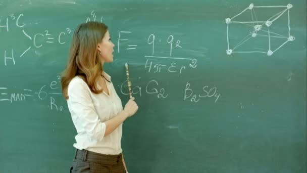 Smiley teacher standing at the blackboard where the chemical formula is written - Materiaali, video