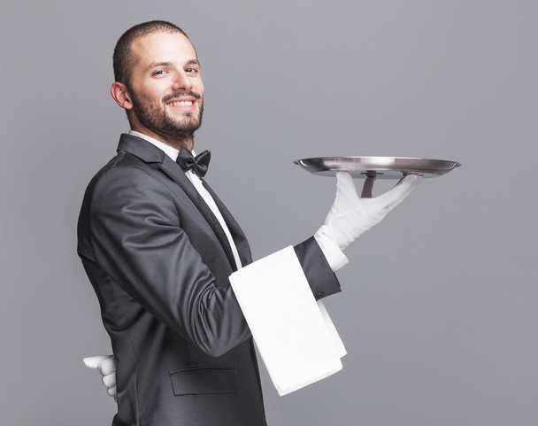 Smiling waiter holding a silver tray - Фото, изображение