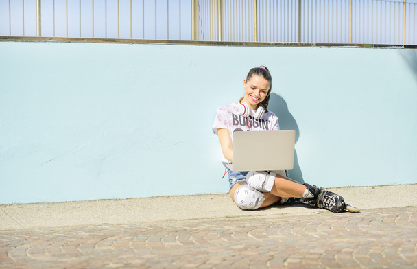 giovane atleta bella ragazza in pantaloncini di jeans corti e pattini a rotelle seduta in riva al mare, che lavora al computer e sorride
 - Foto, immagini