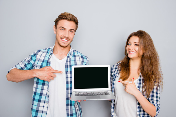 Young couple demonstrating laptop and pointing on screen with co - Zdjęcie, obraz