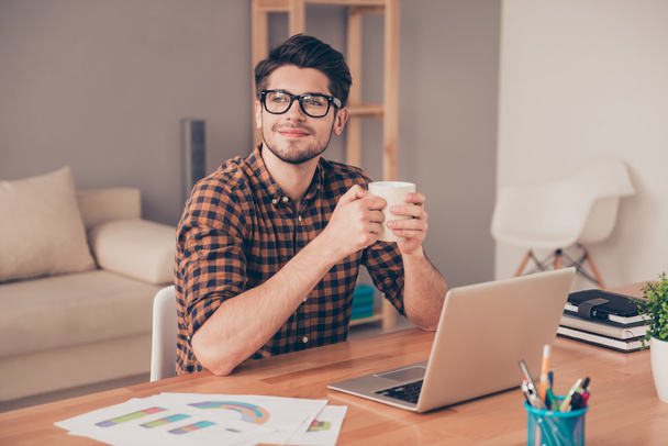 Молодой красивый мужчина в очках пьет кофе в офисе и мечтает
 - Фото, изображение