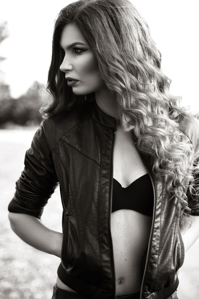 fashion model with long curly hair wearing leather jacket posing - Фото, изображение