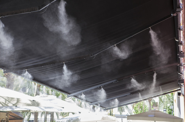 Разбрызгиватели навеса брызгают водой в баре на террасе
 - Фото, изображение