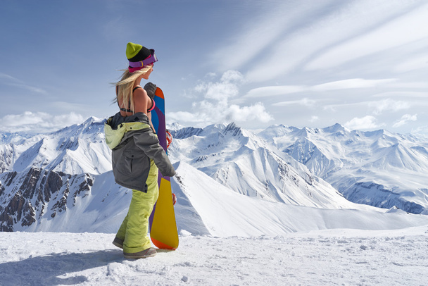 Πίσω όψη του κοριτσιού με πολύχρωμο snowboard κοιτάζοντας μακριά στα βουνά - Φωτογραφία, εικόνα