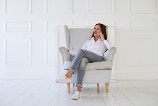 Mujer hablando en el teléfono inteligente mientras está sentada en un sillón
 - Foto, imagen