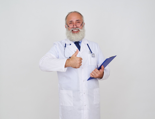 Médico sonriente haciendo bien, gesto con una carpeta y estetoscopio
 - Foto, Imagen