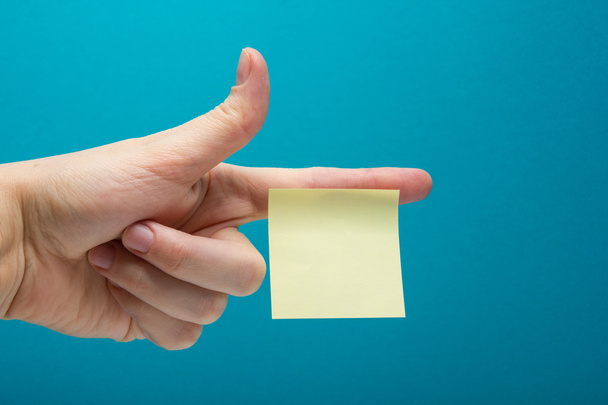 Sticky note, finger up of thumb, yellow reminder on blue background. - Photo, Image