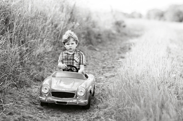 Kleiner Junge fährt großes Spielzeugauto mit einem Bären im Freien. - Foto, Bild
