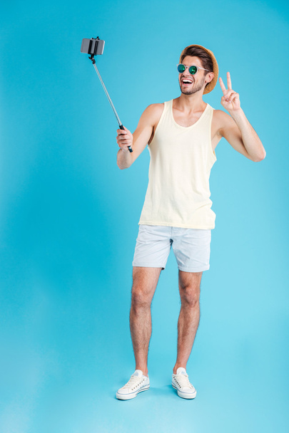 Cheerful young man taking selfie with smartphone and monopod - Fotoğraf, Görsel