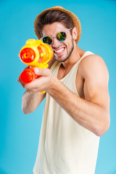 Cheerful young man having fun using water gun - Foto, Bild