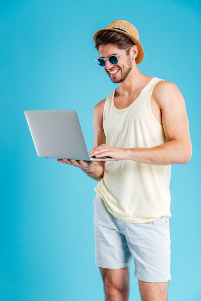 Усміхнений молодий чоловік стоїть і використовує ноутбук
 - Фото, зображення