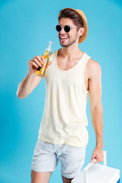 Cheerful young man holding cooler bag and drinking beer - Foto, Bild