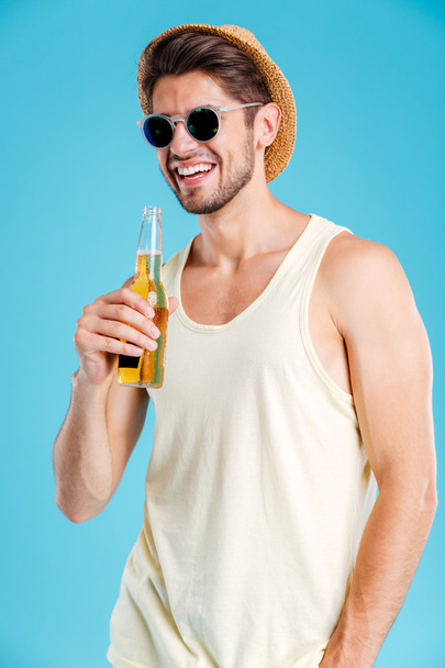 Joven alegre en gafas de sol de pie y bebiendo cerveza
 - Foto, Imagen