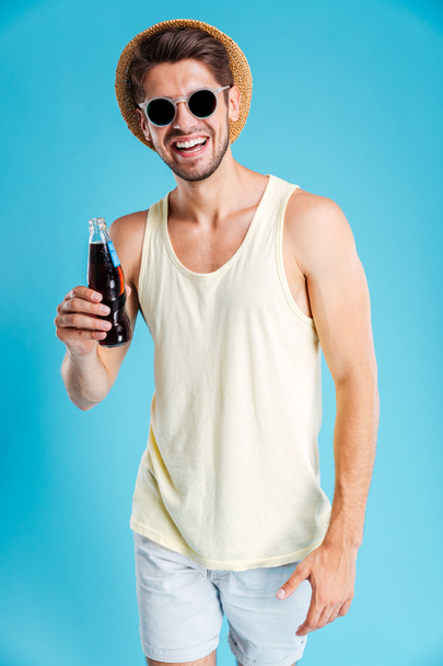 Cheerful young man in hat and sunglasses drinking soda - Фото, зображення