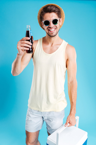 Smiling young man holding cooling bag and bottle of soda - Fotoğraf, Görsel