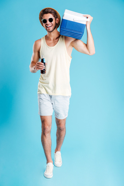 Man with cooling bag on shoulder walking and drinking soda - Foto, afbeelding