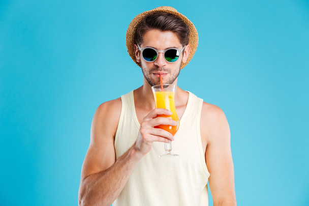 Attractive young man in hat and sunglasses drinking orange juice - Valokuva, kuva