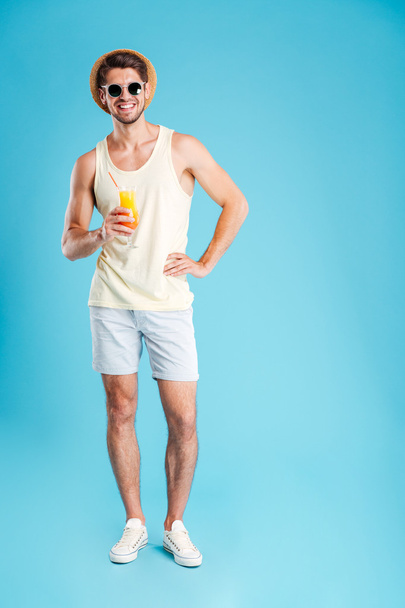Cheerful young man standing and holding glass of orange juice - Foto, imagen