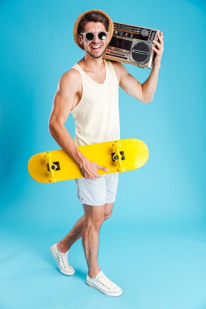 Smiling man with yellow skateboard walking and holding old boombox - Photo, image