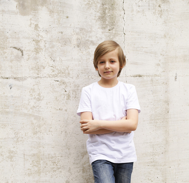 ジーンズと白いシャツの壁の背景にポーズかわいい金髪の少年 - 写真・画像