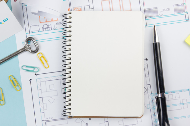 Real estate concept. Blank white notebook on architectural desk table blueprint background with key, pen, small house, office supplies. Copy space for ad text, top view. - Photo, Image