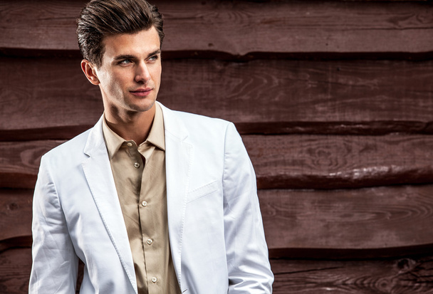 Portrait of young beautiful fashionable man in white costume against wooden wall - Photo, image