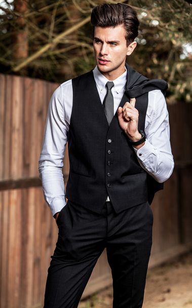 Elegant handsome man in classical suit poses near wooden fence - Photo, Image