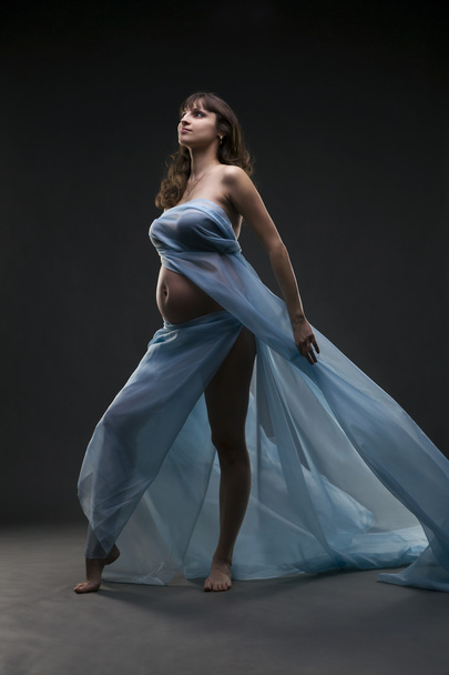 Young beauty and sexy caucasian pregnant woman with blue silk on gray studio background - Foto, Imagen