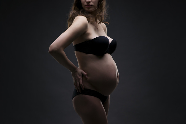 Young beauty and sexy caucasian pregnant woman in black lingerie on gray studio background - Valokuva, kuva